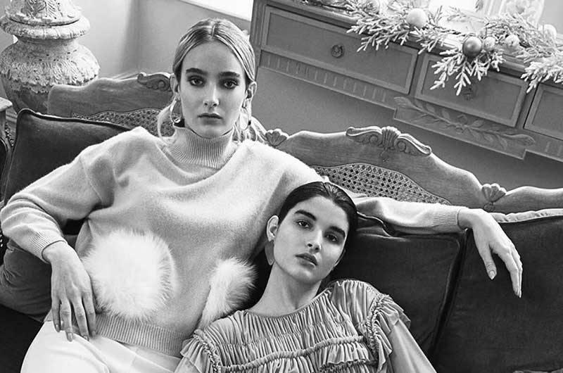 Black and white image of two girls sitting on a couch wearing statement earrings